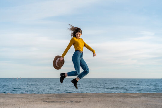 Young woman with sun hat jumping while enjoying against sea