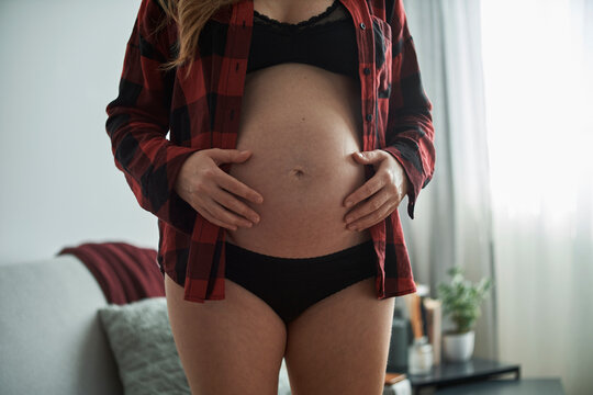 Close-up of pregnant woman with hands on stomach standing at home