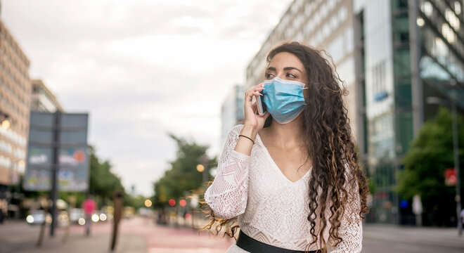 Woman wearing mask talking over mobile phone while standing in city