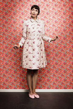 Fototapeta Beautiful woman looking away while standing against floral wallpaper in studio