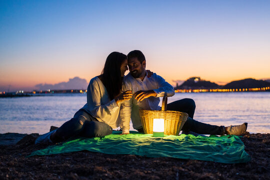 Romantic couple with drinks sitting at beach against clear sky during dusk