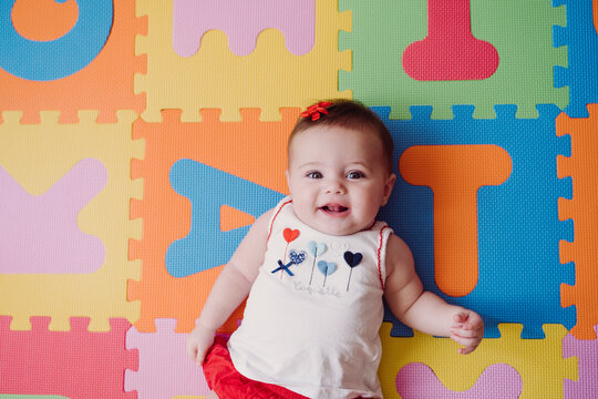 Cute baby girl relaxing on colorful alphabetical puzzle playmat at home