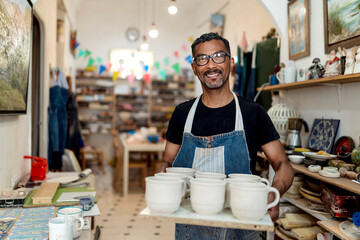 Smiling male artist holding potteries while standing in workshop
