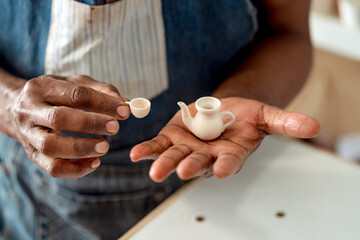 Close-up of male artist holding miniature cup and teapot in workshop