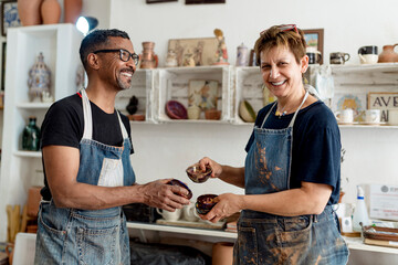 Smiling artists holding ceramics while standing in workshop