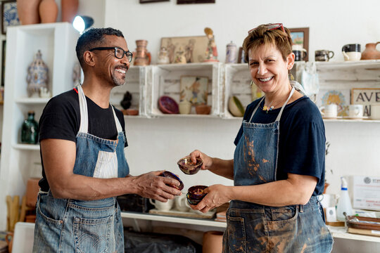 Smiling artists holding ceramics while standing in workshop