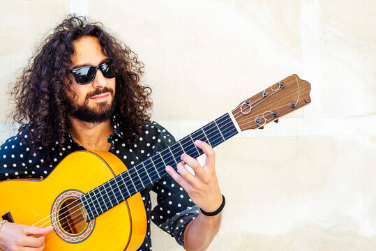 Man with sunglasses playing guitar while standing against wall