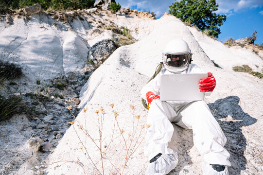 Male astronaut using laptop while sitting on mountain