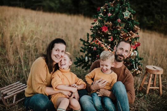 Cheerful family with Christmas tree sitting on land during sunset