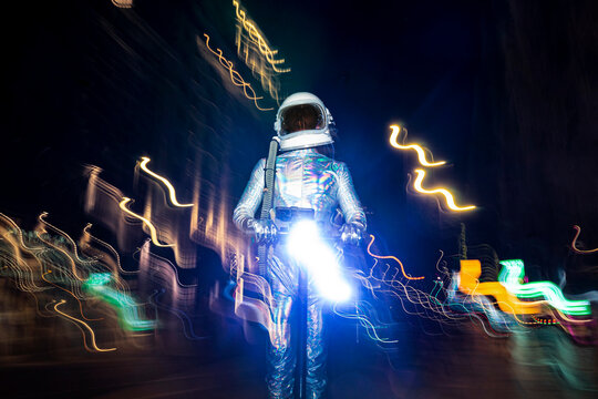 Male astronaut wearing space suit standing amidst light paintings on street at night