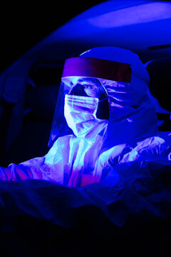 Man wearing protective suit driving illuminated ambulance at night
