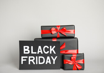 Gift boxes and sheet of paper with words Black Friday on light grey background