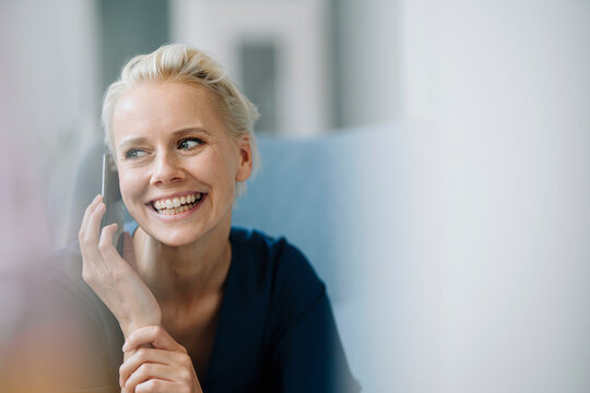 Close-up of cheerful businesswoman talking over smart phone while sitting in office