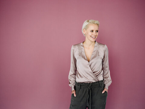 Smiling female entrepreneur with hands in pockets looking away while standing against purple background