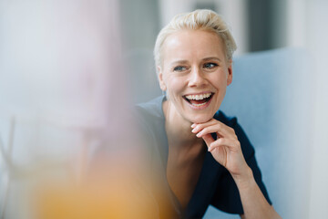 Close-up of businesswoman with hand on chin laughing while sitting in office