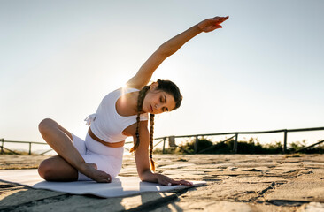 Young woman with eyes closed exercising on mat against clear sky at sunset