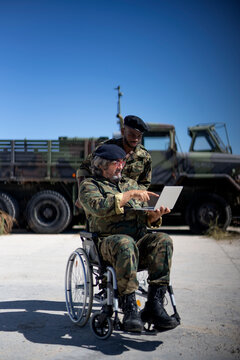 Disabled military officer working on laptop with colleague during sunny day