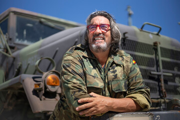 Smiling army soldier with arms crossed leaning on military truck during sunny day