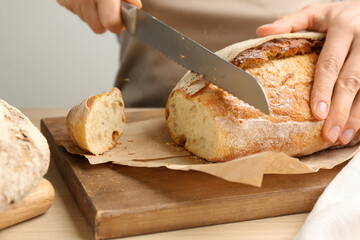 Woman cutting freshly baked bread at wooden table, closeup