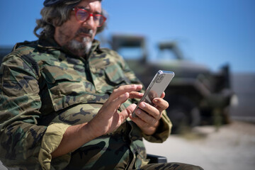 Military officer text messaging on smart phone while sitting on wheelchair during sunny day