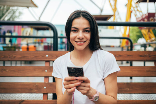 Beautiful woman with smart phone sitting on bench at amusement park