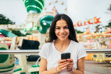 Close-up of smiling young woman using smart phone against amusement park ride