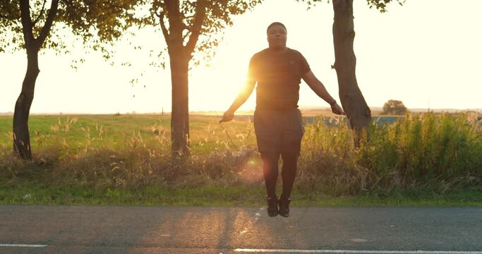 Young handsome concentrated male working out with jump rope outdoors on sunset. African American man doing exercises and jumping on street alone. Weight loss concept. Sport lifestyle