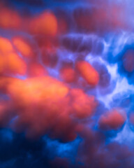 Obraz premium Red and orange clouds at sunset or sunrise with very curious shapes. Mammatus clouds. Strange and artistic sky clouds vertical background.