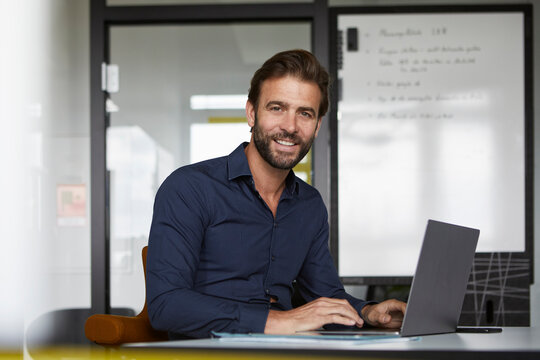 Smiling man working on laptop while sitting by desk in office