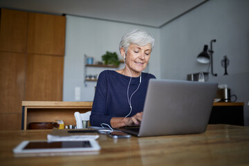 Active senior working on laptop while listening music sitting at home