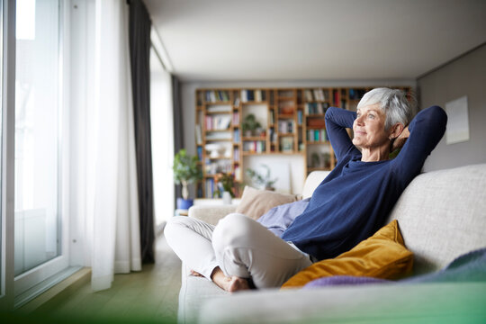 Senior woman with hands behind head with cross legged sitting on sofa at home