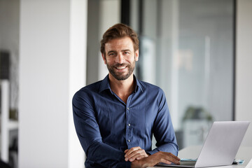 Smiling businessman using laptop while standing at desk in office