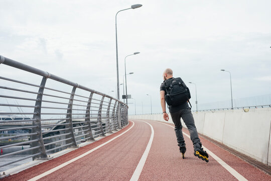 Young man with backpack inline skating on bridge against sky