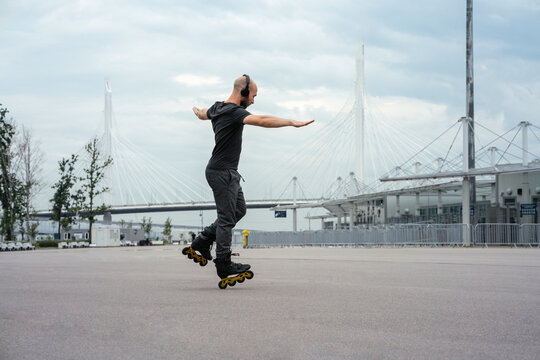 Man with arms outstretched listening music while inline skating on road against cloudy sky