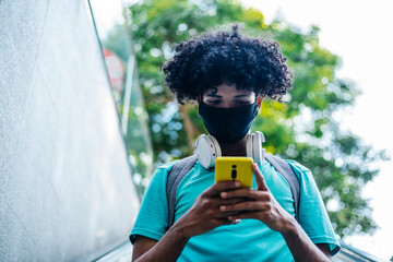 Young man with wearing protective face mask text messaging on smart phone while standing on escalator