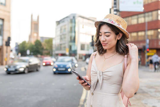 Woman smiling while text messaging on smart phone standing in city