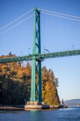 A close up view of the Lion's Gate Bridge and the Stanley Park in the background taken from a boat on the water.