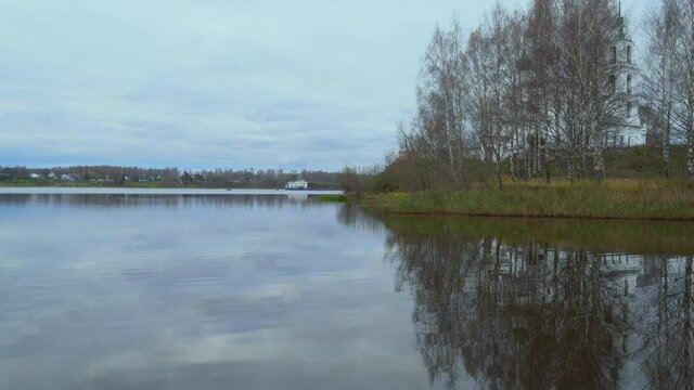 Holy Trinity Church in the village of Dievo Gorodishche, Yaroslavl region, Russia. A floating barge with a wood in the background. Reflection of the Church and trees in the quiet backwater of the Volg