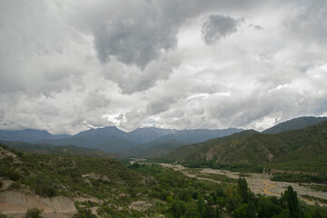 Panorama view of the green forest foliage, mountains and yellow river flowing across the valley, under a dramatic cloudy sky. 