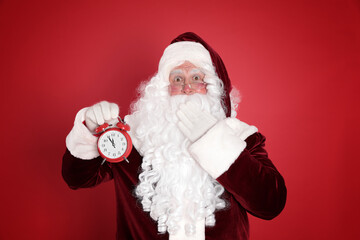 Santa Claus holding alarm clock on red background. Christmas countdown