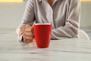 Woman with red cup at table indoors, closeup