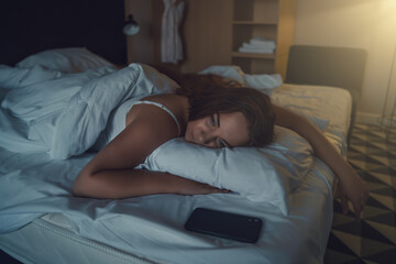 Beautiful young woman lying on her stomach on bed, unable to sleep, insomnia or anxiety due to stress.