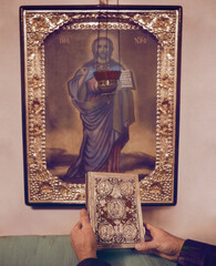 Bible in man’s hands in front of the icon of Jesus Christ. The Cathedral of the Nativity of the Blessed Virgin (1752-1763). Kozelets. Chernihiv Region. Ukraine.