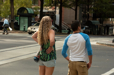 A couple wait to cross the street in an urban setting.