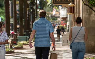 A man and woman stroll through downtown carrying a bag. 