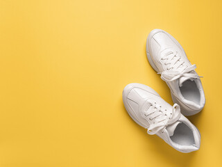 Pair of white chunky sole sneakers over an yellow amber paper background. New unisex tied laces shoes for active lifestyle, fitness and sports. Copy space.