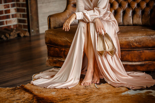 cute girl in a long dress sits barefoot on a leather sofa. Brick background
