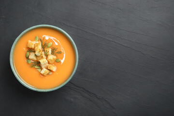 Delicious pumpkin soup in bowl on black table, top view. Space for text
