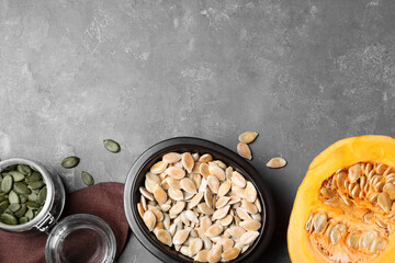 Flat lay composition with full bowl of pumpkin seeds on grey table, space for text