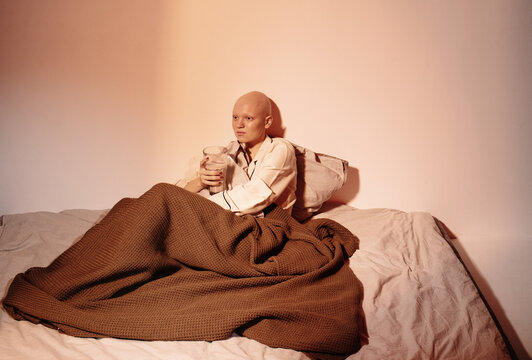 Bald female with glass of cocoa sitting in bed